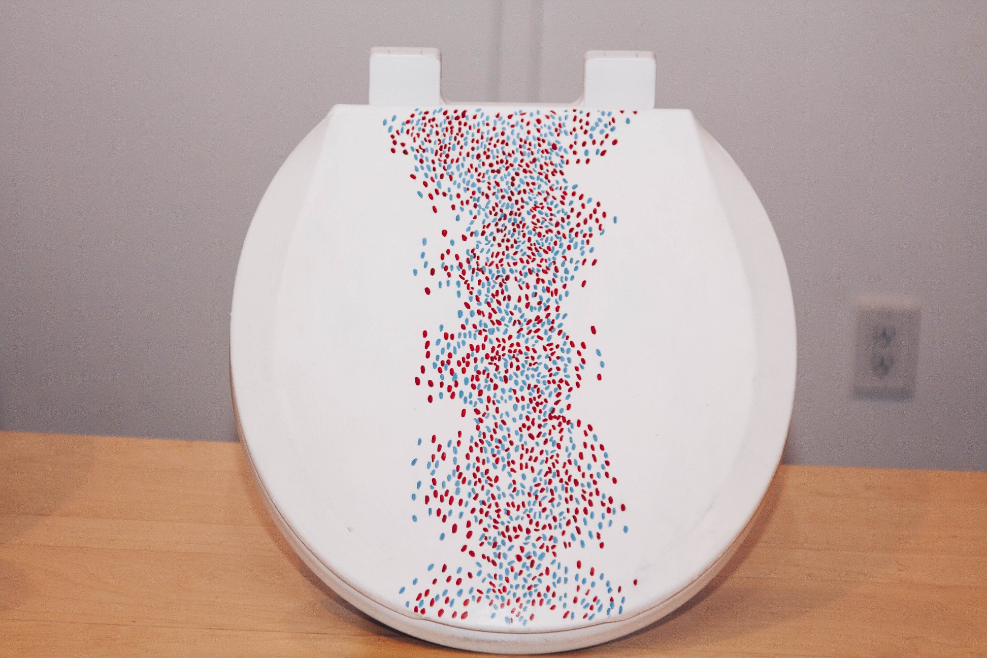 A white toilet with a flock of red and blue dots elegantly moving up the middle of the toilet seat.